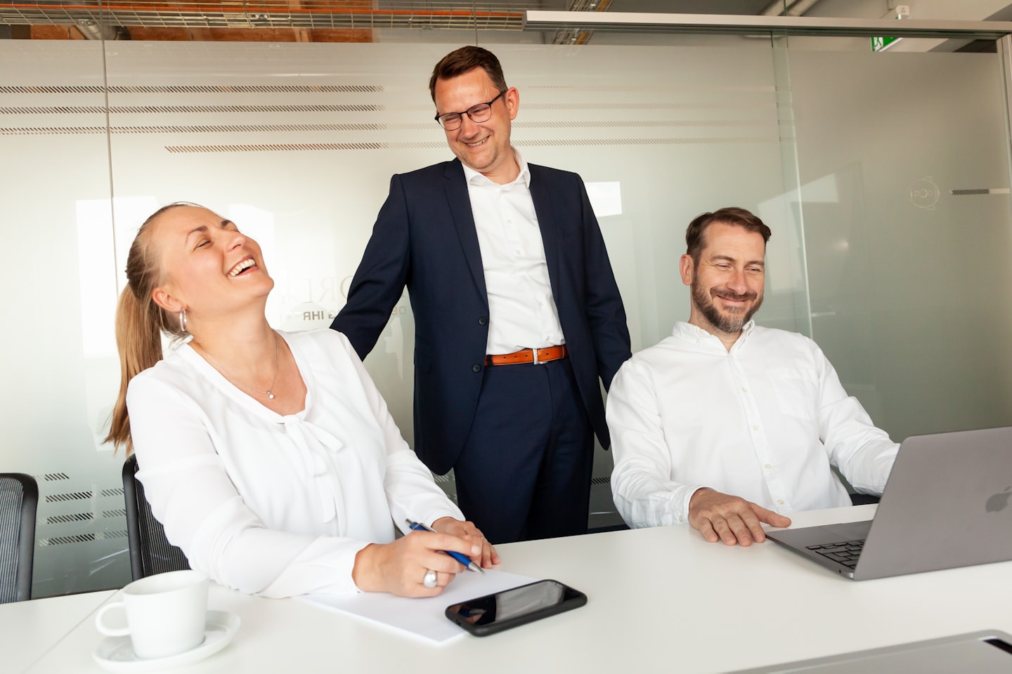 Tre professionisti sorridenti collaborano attorno a un tavolo in un ufficio moderno.